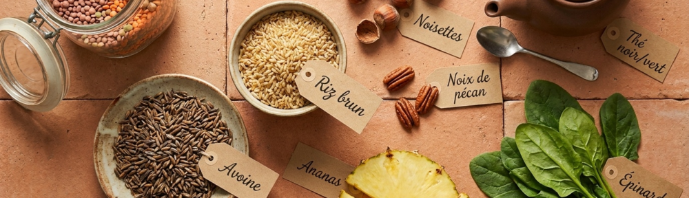 Photographie alimentaire éditoriale hyper-réaliste d'un flat-lay des sources naturelles de manganèse sur surface terre cuite méditerranéenne : flocons d'avoine, riz brun, pois chiches, lentilles, noisettes, noix de pécan, thé vert en vrac, ananas frais et épinards frais